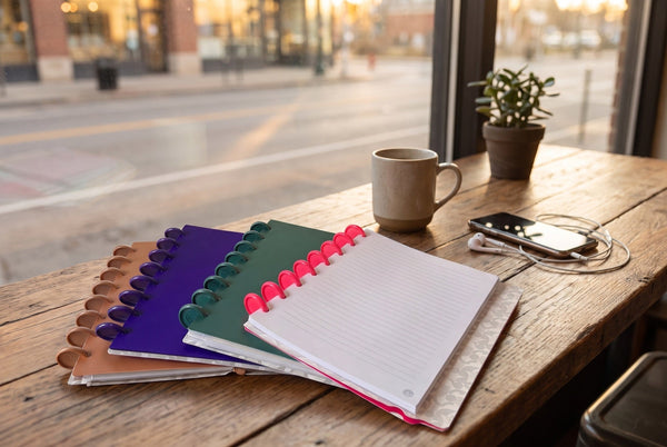 Carnets Mylibup en éventail sur une table de café près d'une vitrine, avec une tasse, un téléphone et des écouteurs, lumière de fin d'après-midi