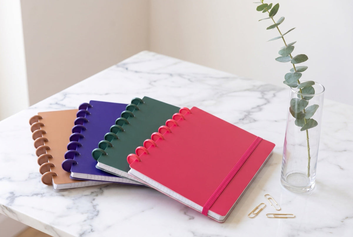 Carnets Mylibup en éventail sur une table en marbre, avec une branche d'eucalyptus dans un vase en verre et deux trombones dorés